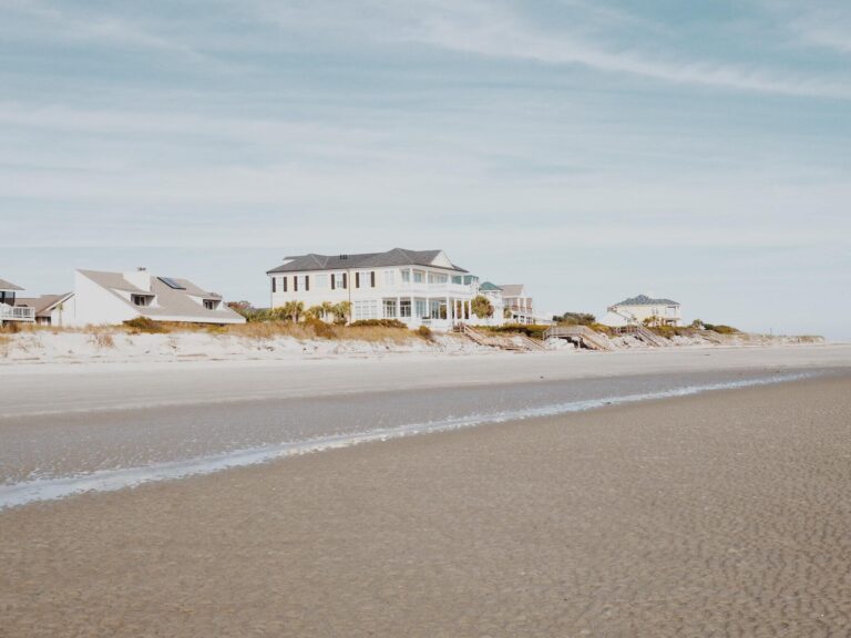 A view from the shore of a beach looking back at three houses behind dunes