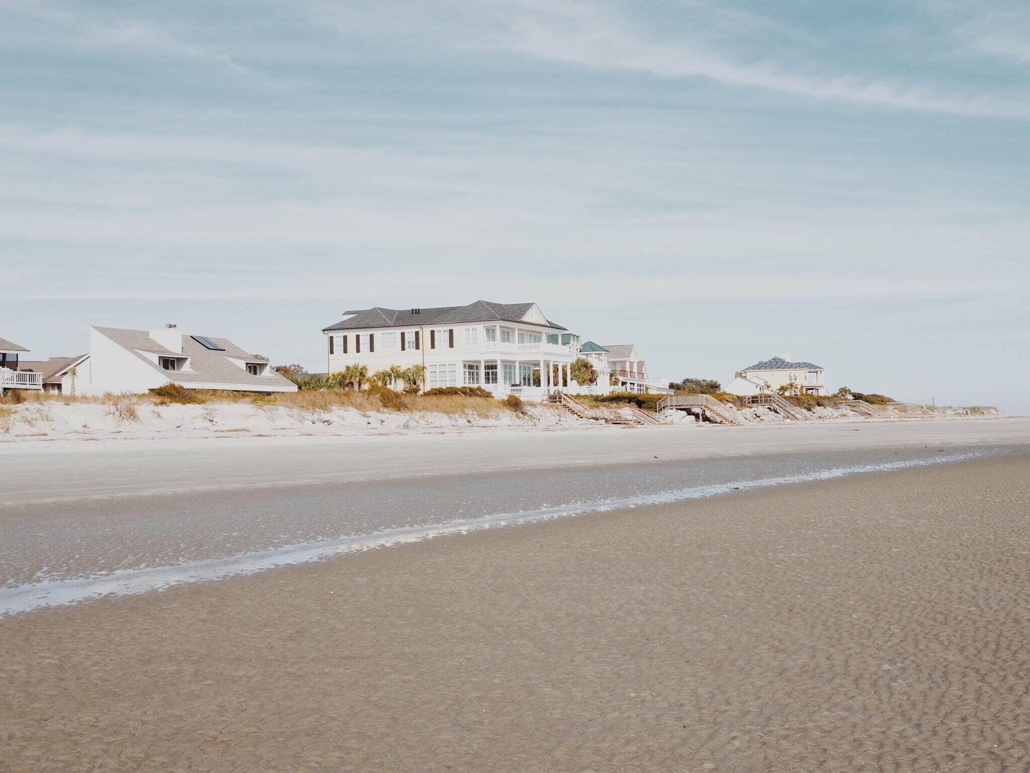 A view from the shore of a beach looking back at three houses behind dunes