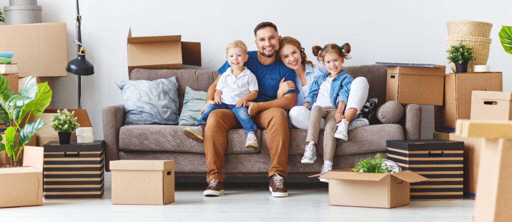 A happy family sitting on a couch with moving boxes surrounding them