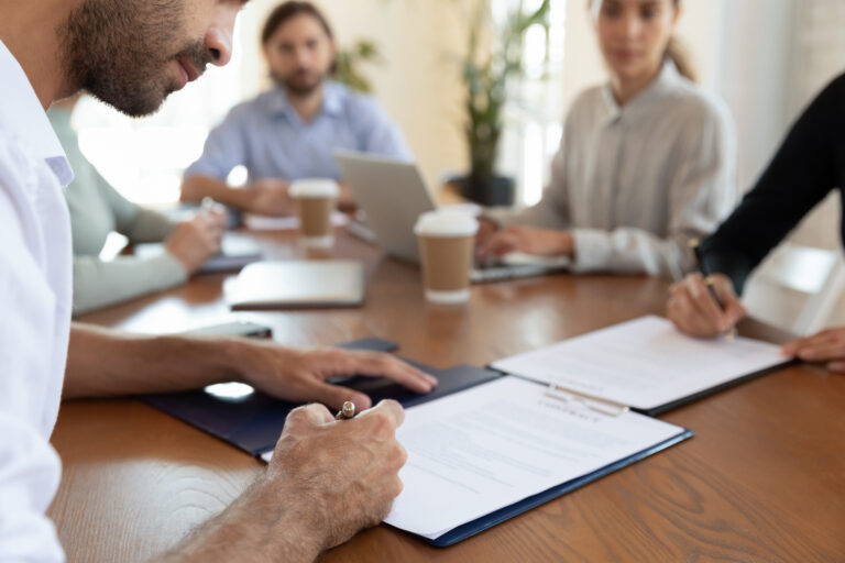 Man writing on a contract with people sat around him at a table