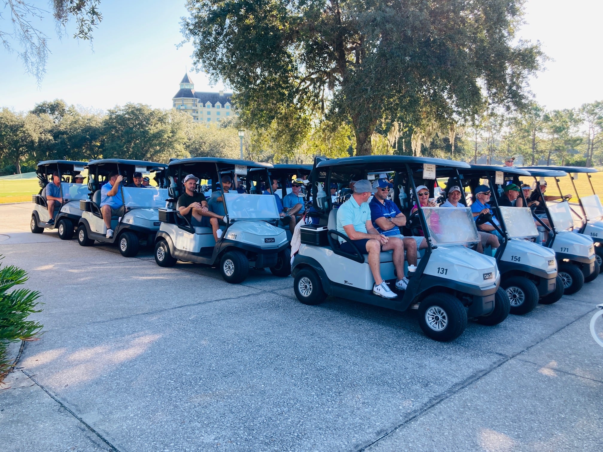 Multiple golf carts next to each other with people in them with a golf course in the background before a golf tournament